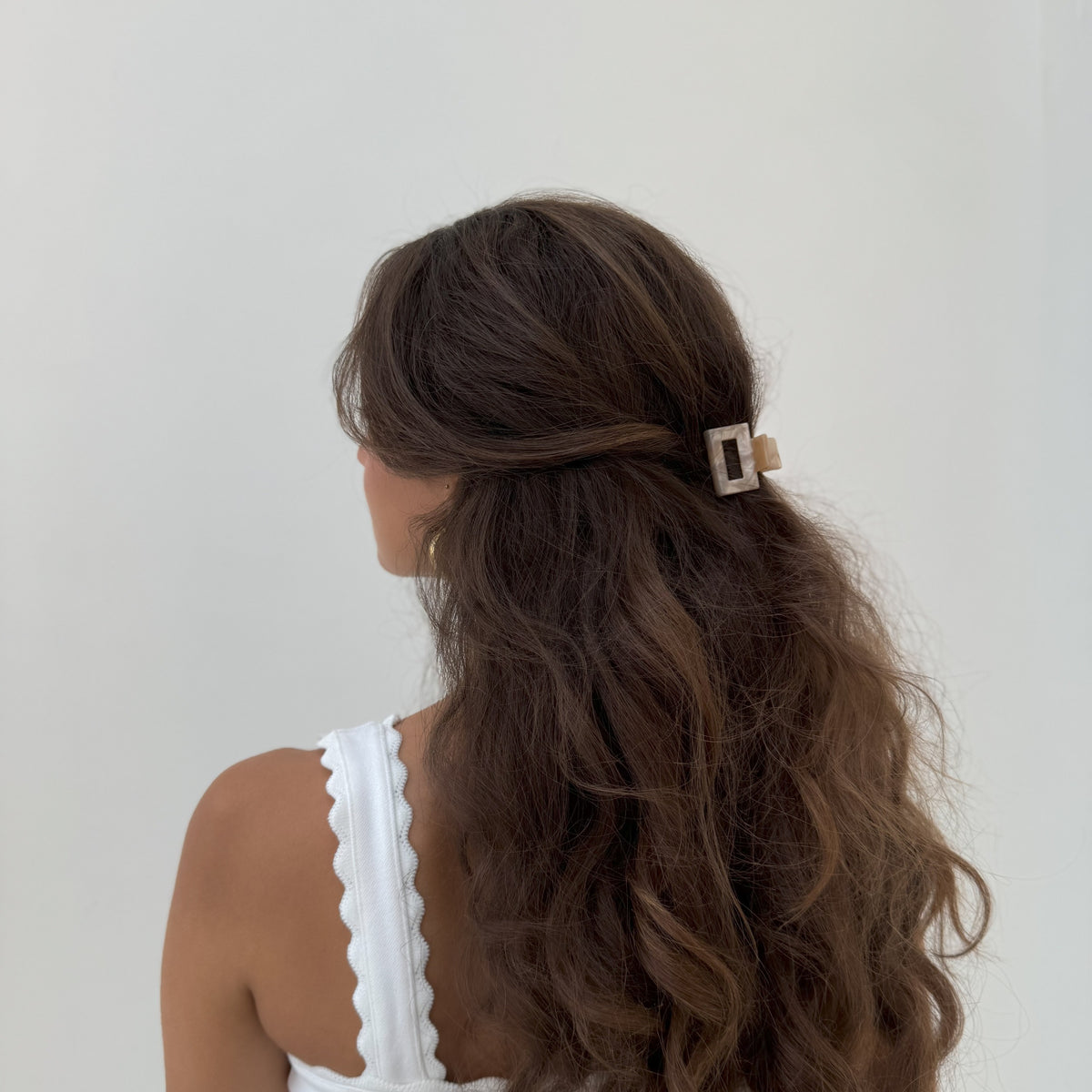 Woman with long brown wavy hair wearing a caramel acetate mini square claw clip in a half-up style, seen from behind