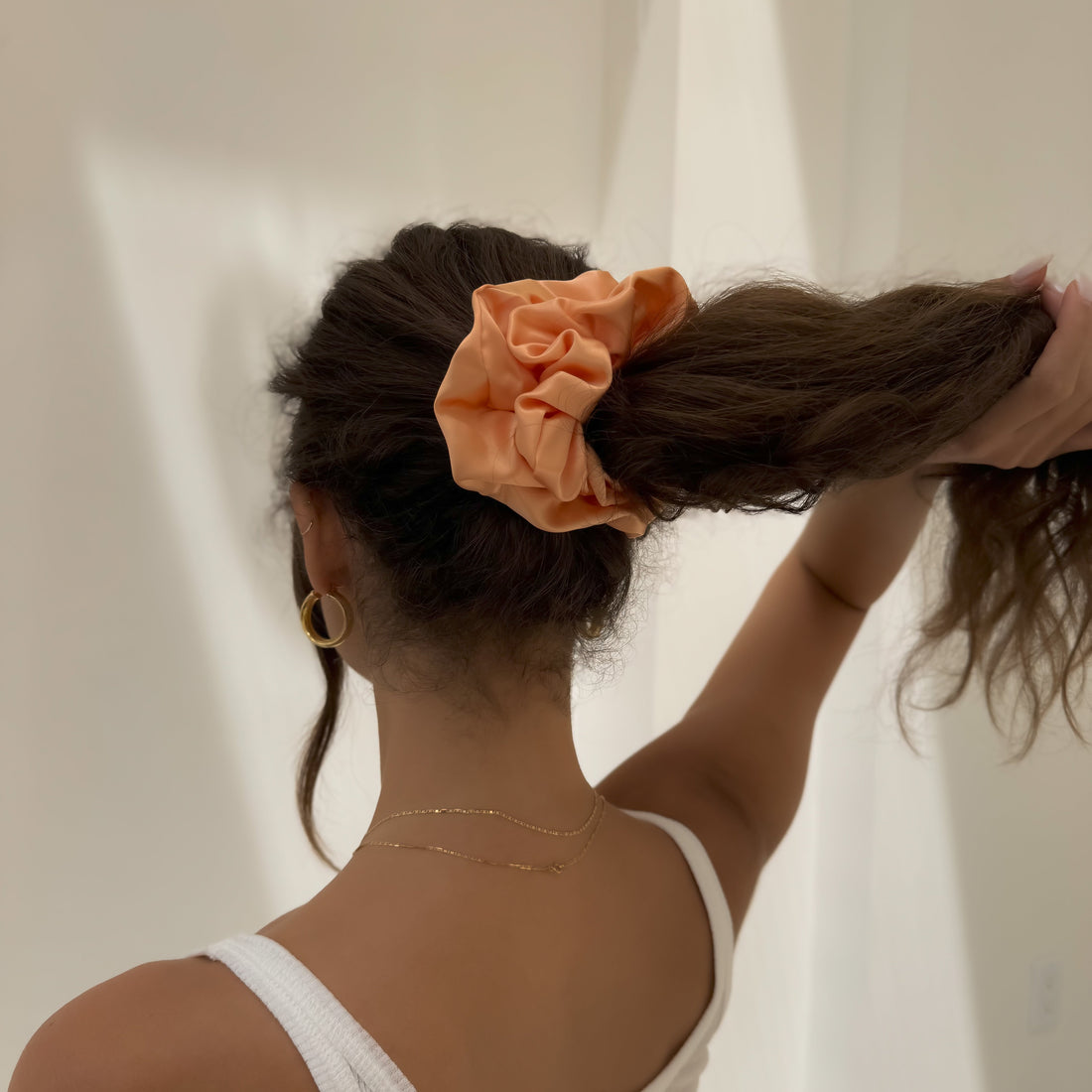 Woman tying hair with peach scrunchie